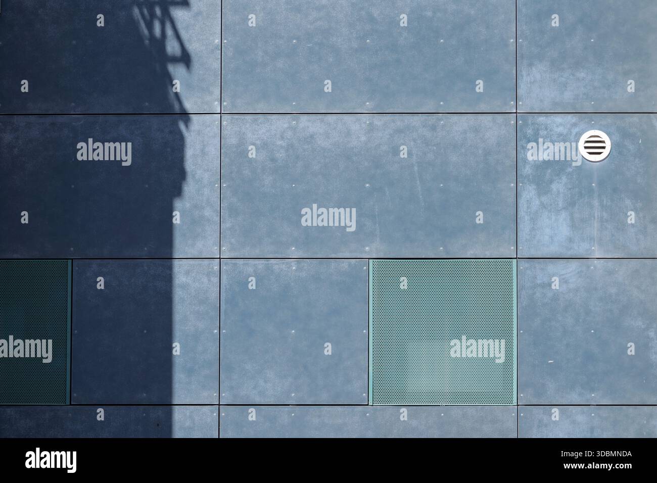 Geometry in Shade, una facciata di pannelli blu con una forte ombra, una bocchetta rotonda e una bocchetta quadrata, che evidenziano l'equilibrio geometrico tra luce, texture e forma architettonica. Foto Stock