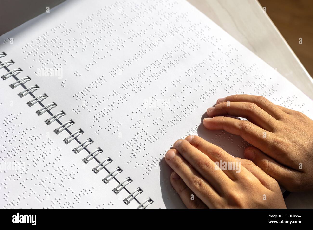Bambino ipovedente che legge un libro in Braille in modo indipendente. Educazione inclusiva e apprendimento tattile per bambini con ipovedenza o con esigenze particolari. Foto Stock
