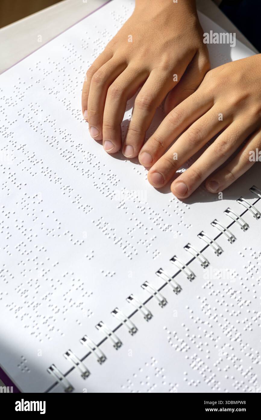 Bambino ipovedente che legge un libro in Braille in modo indipendente. Educazione inclusiva e apprendimento tattile per bambini con ipovedenza o con esigenze particolari. Foto Stock