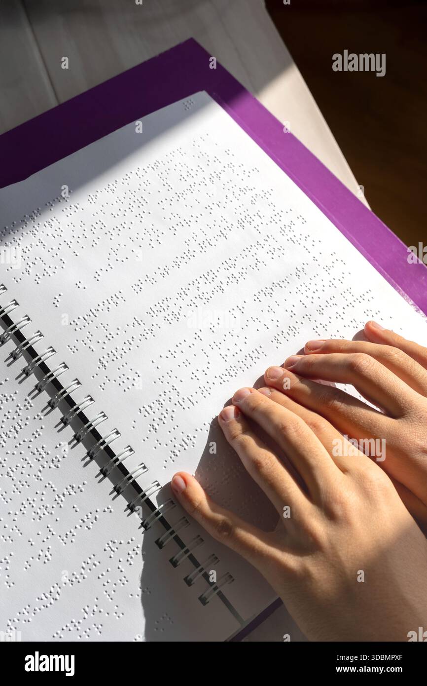 Bambino ipovedente che legge un libro in Braille in modo indipendente. Educazione inclusiva e apprendimento tattile per bambini con ipovedenza o con esigenze particolari. Foto Stock