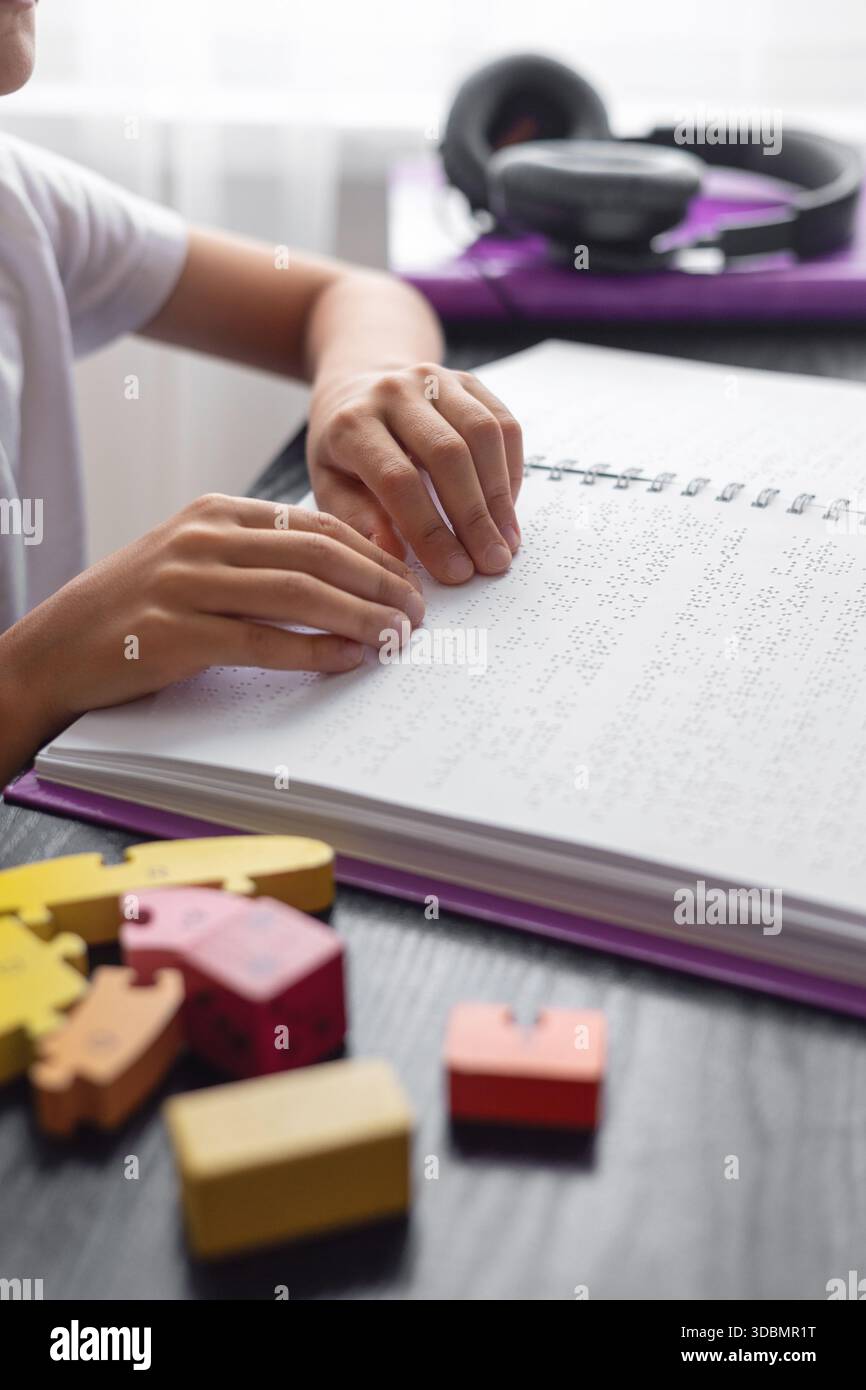 Bambino ipovedente che legge un libro in Braille in modo indipendente. Educazione inclusiva e apprendimento tattile per bambini con ipovedenza o con esigenze particolari. Foto Stock