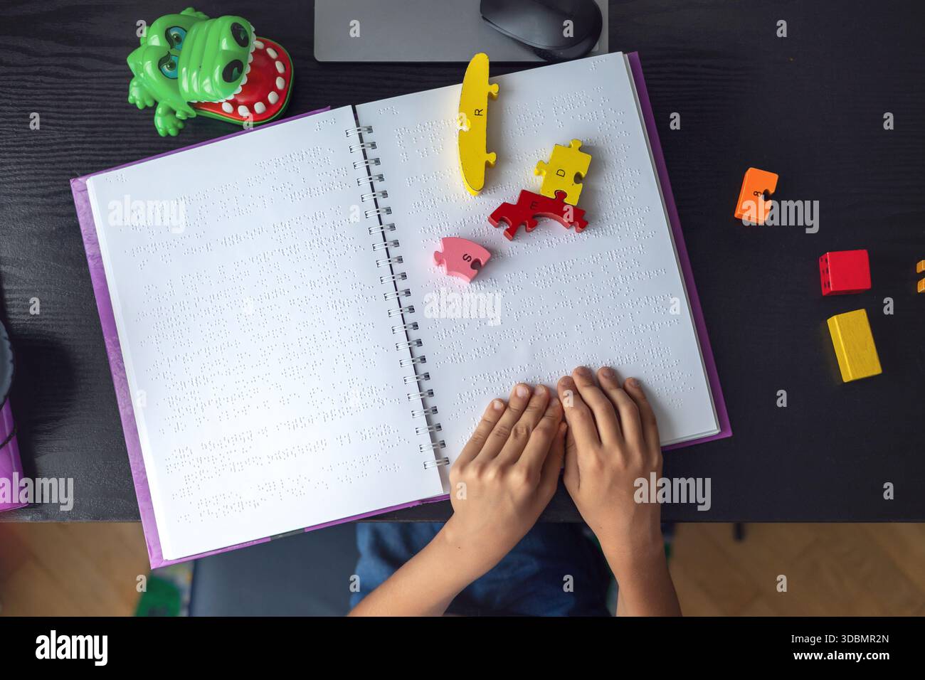 Bambino ipovedente che legge un libro in Braille in modo indipendente. Educazione inclusiva e apprendimento tattile per bambini con ipovedenza o con esigenze particolari. Foto Stock