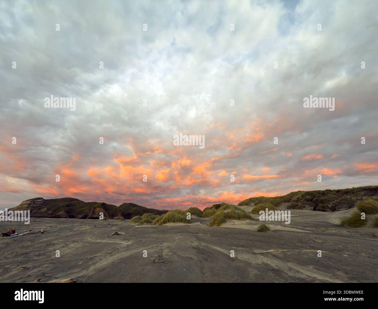 Vista di una spiaggia di sabbia ferma che incontra aspre scogliere sotto un cielo spettacolare che si accendono con sfumature di tramonto sulla spiaggia di Wharariki, Pūponga, regione di Tasman, nuova Zelanda Foto Stock