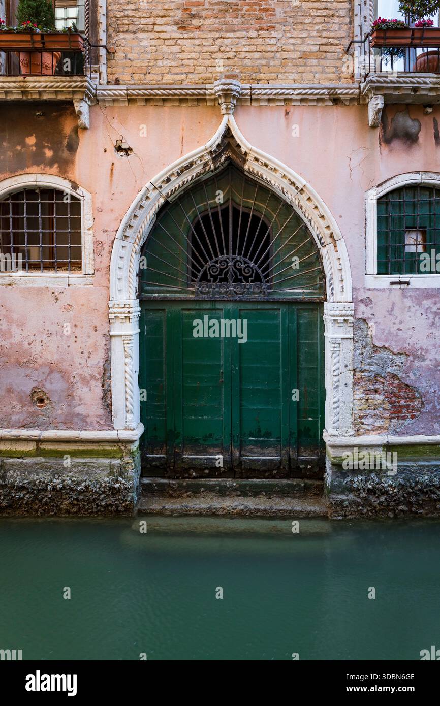 Porta gotica intemprata e ornata che si apre sul canale. Finestre con griglie su ciascun lato e ferro a ventaglio nella parte superiore della porta, balconi con fiori sopra. Foto Stock