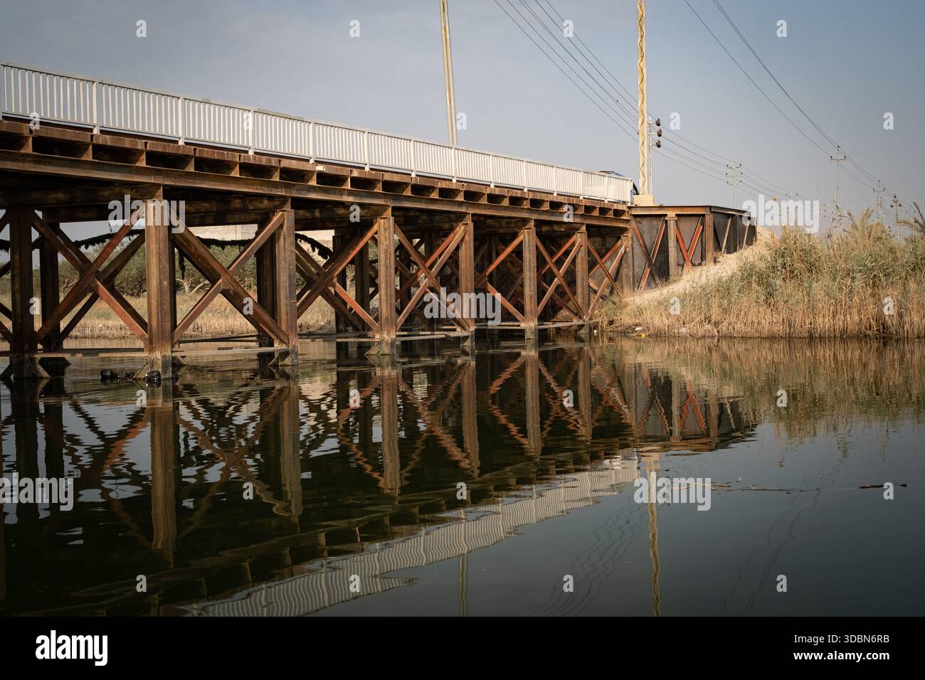 Lungo ponte in legno che si estende su un ampio canale navigabile, sostenuto da cavalletti in legno, con veicoli parcheggiati sotto la struttura. Foto Stock