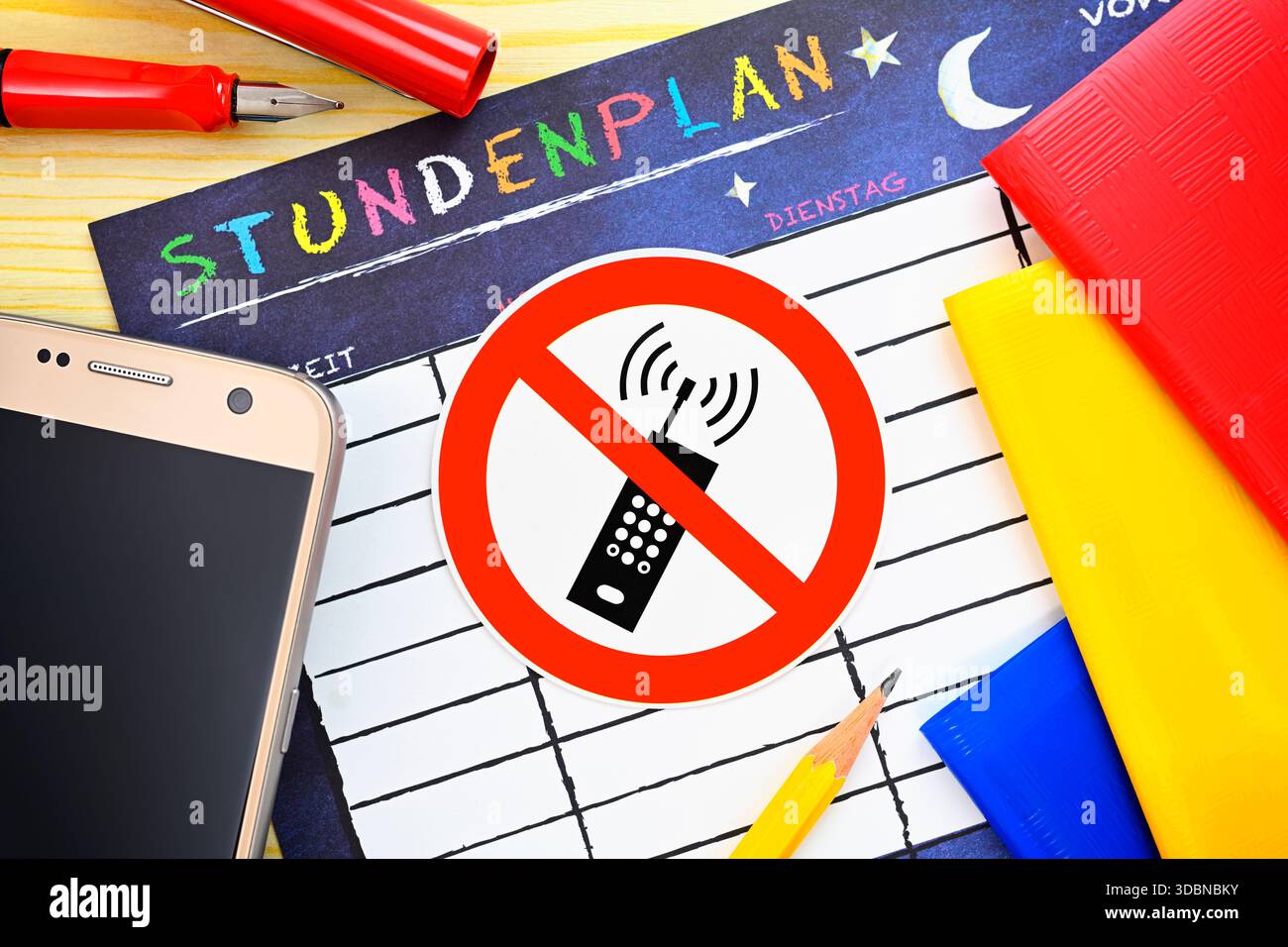 Telefono cellulare con cartello di divieto circondato da utensili scolastici, foto simbolica per il divieto di cellulare a scuola Foto Stock
