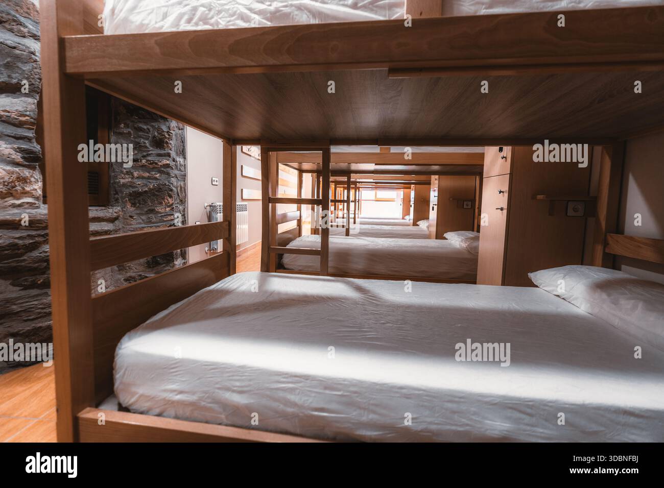 Vista interna del dormitorio dell'ostello attraverso letti a castello in legno, camera da letto condivisa pulita con materassi e cuscini, sistemazione economica per viaggi, Foto Stock