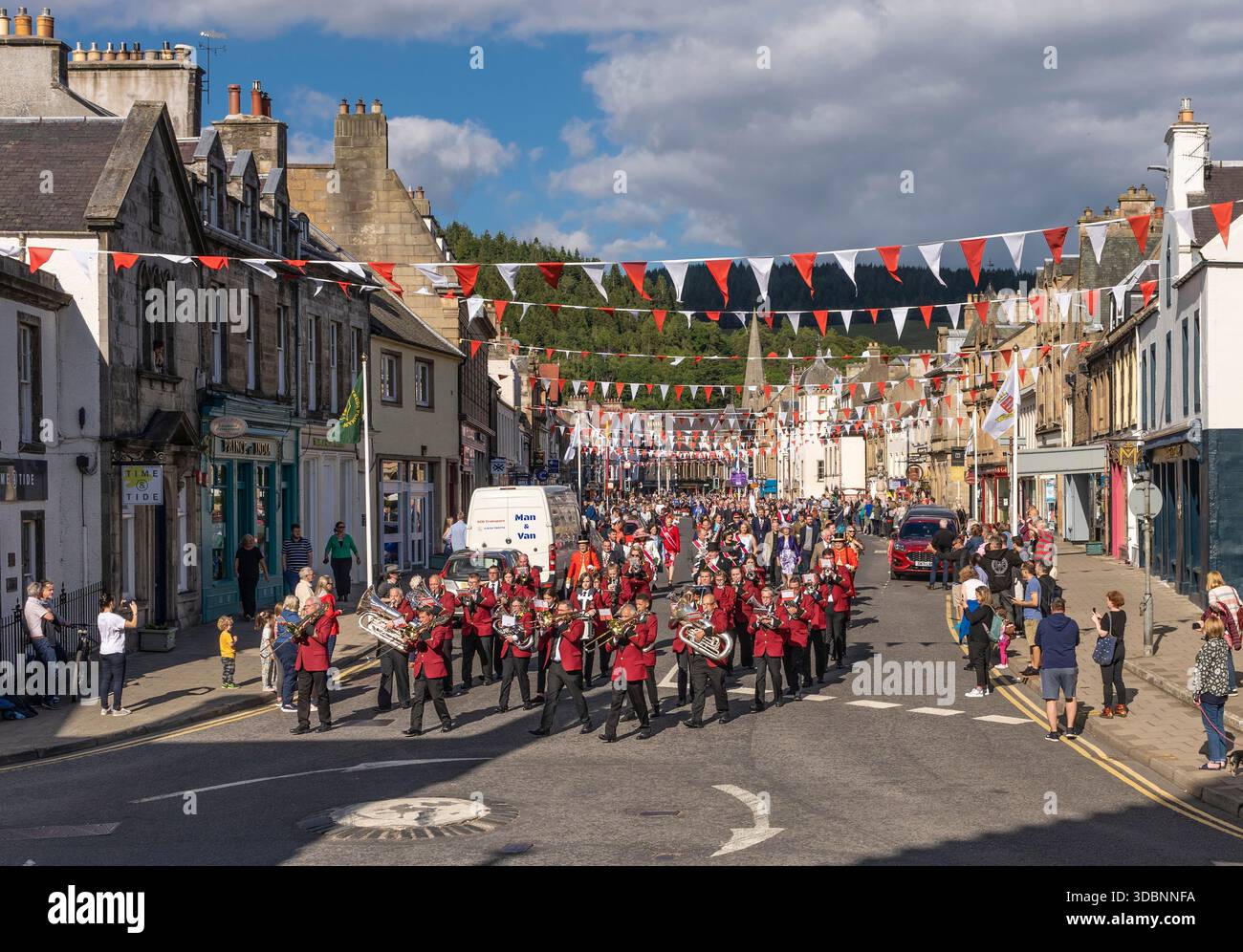 Vivace sfilata di strada con una banda a pipa rossa uniforme, striscioni e una folla vivace a Peebles. Foto Stock