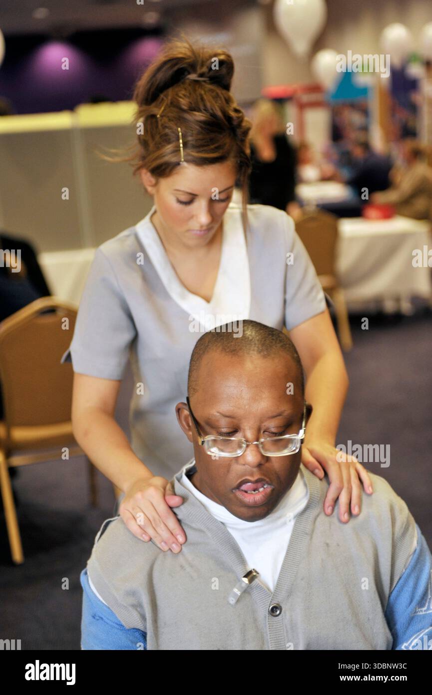 Un massaggiatore che offre massaggi sul posto di lavoro agli impiegati. Foto Stock