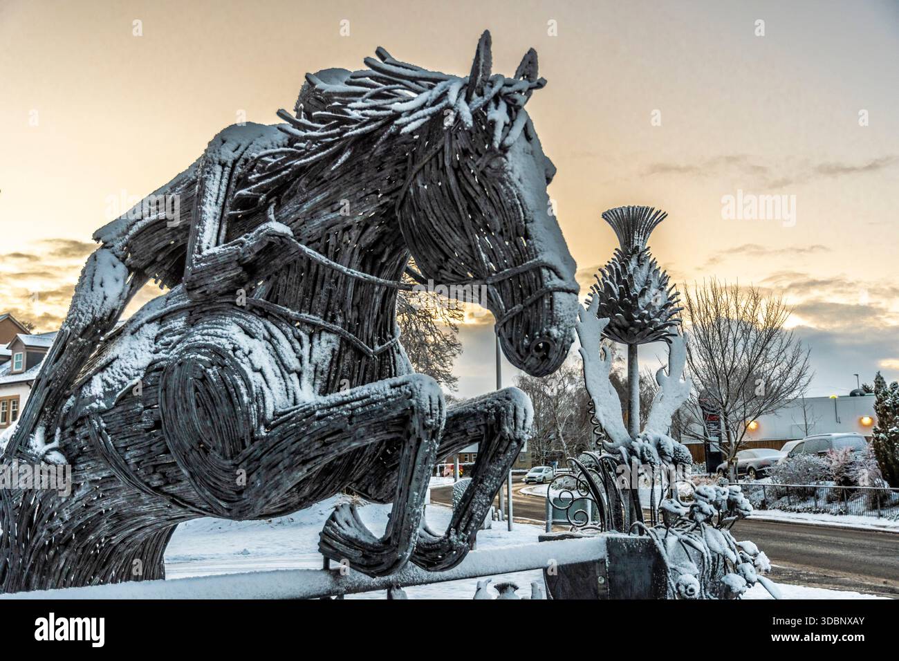 Una grande scultura di cavallo in legno coperta di neve, allestita all'aperto durante un tramonto invernale. Foto Stock