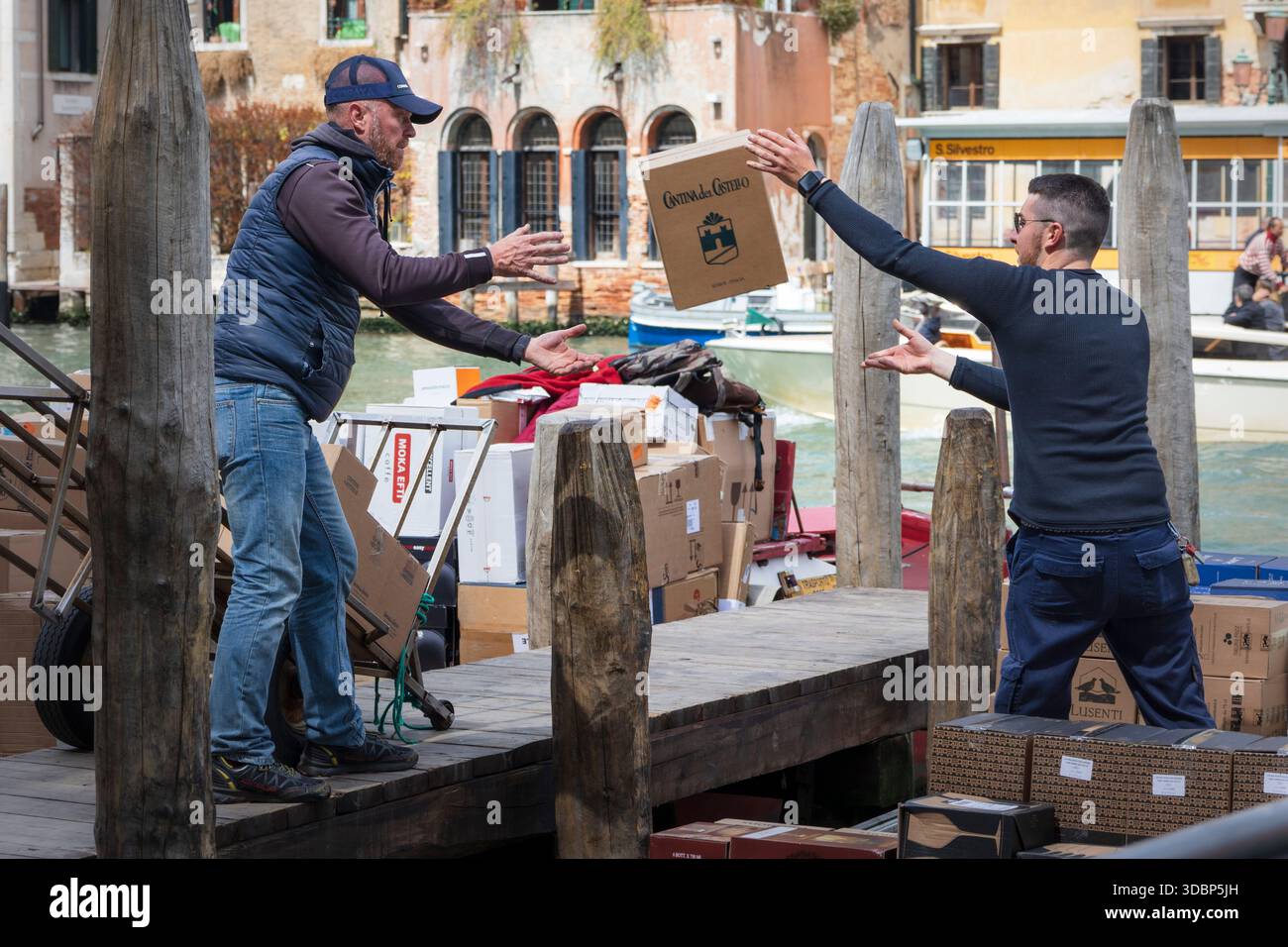 Le scatole vengono trasferite dalla barca al tram da due uomini per la consegna a piedi a Venezia. Canale sullo sfondo. Foto Stock