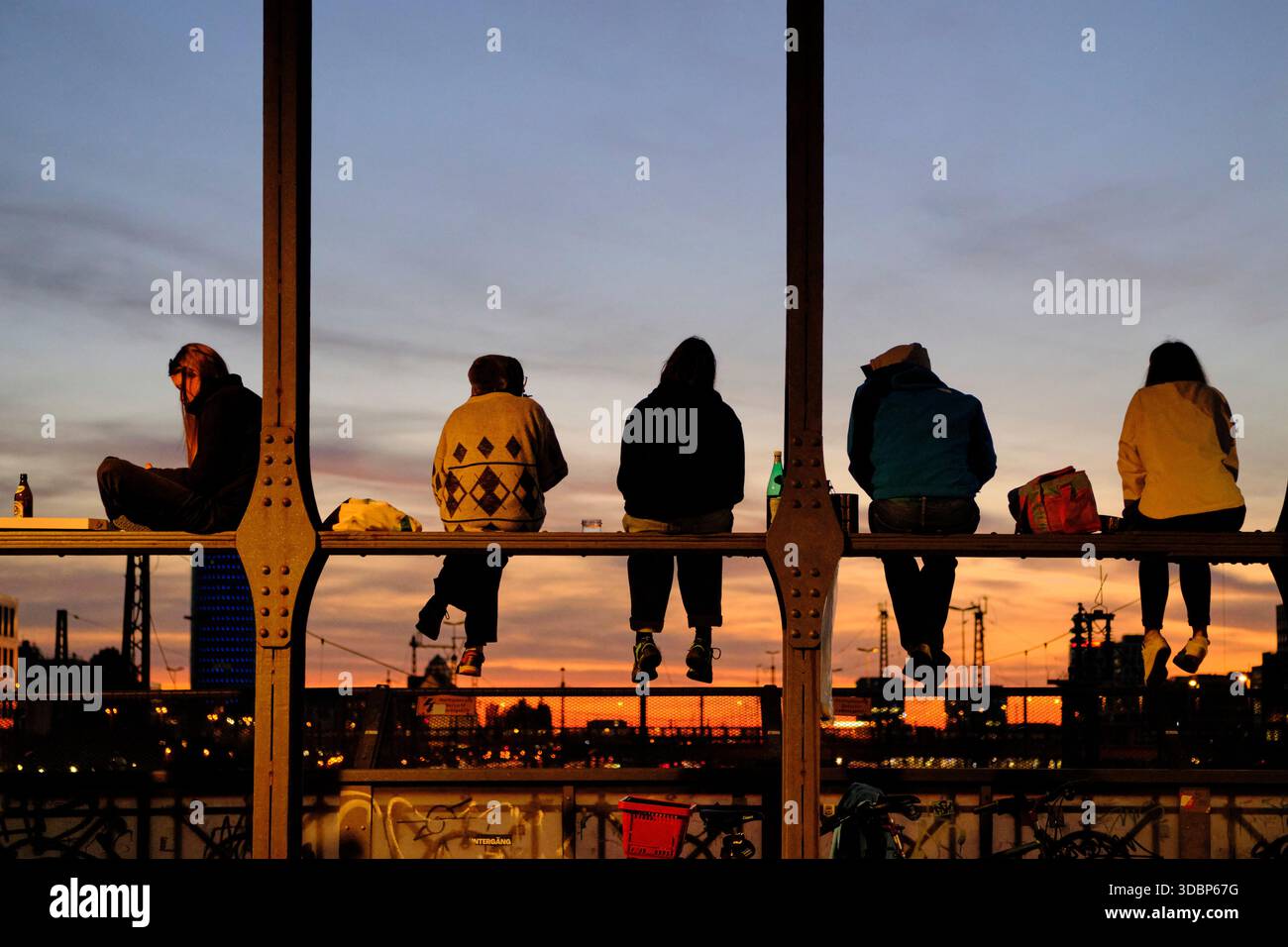 Le persone si siedono a Hackerbrücke a Monaco e si godono il tramonto. Specialmente in estate, questo luogo è ora conosciuto oltre i confini della città per un soleggiato in un'atmosfera urbana. I visitatori si siedono sulle traverse dello storico ponte e ammirano verso ovest il tramonto. Sono invitati a portare le proprie bevande o cibo. Foto Stock
