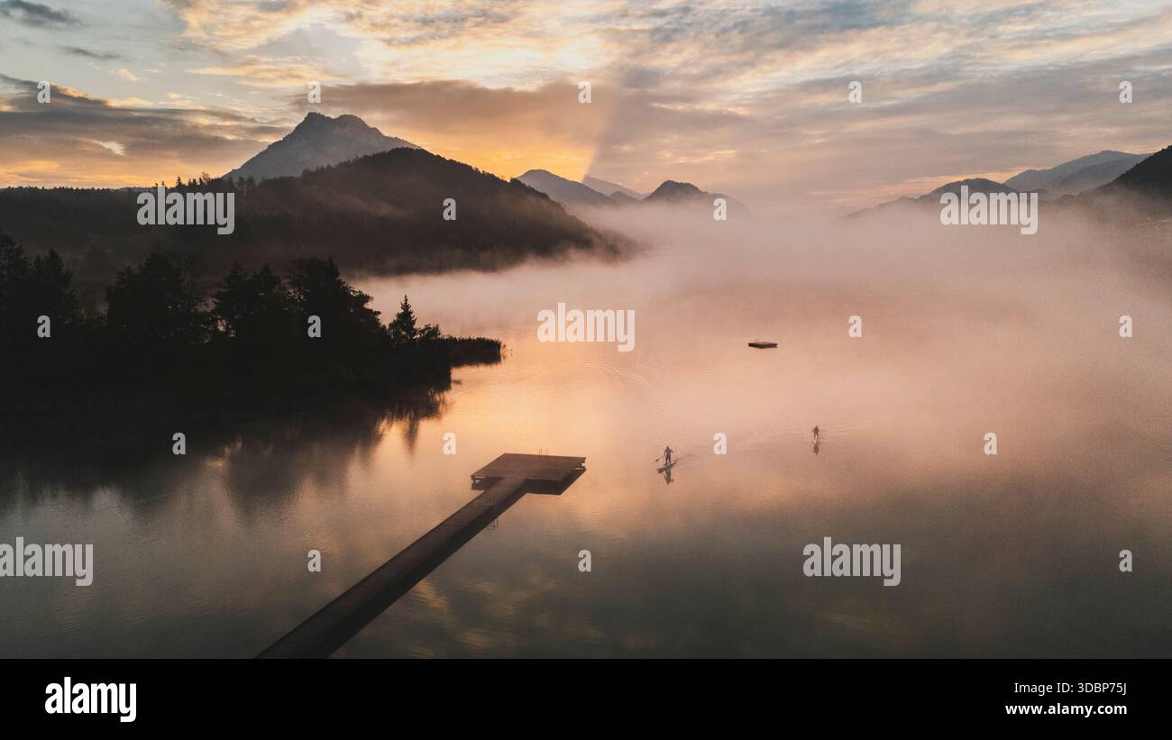 SUP - sali a pagaia all'alba e nelle mattine nebbiose sul Fuschlsee autunnale nella regione Salzkammergut di Salisburgo. Foto Stock