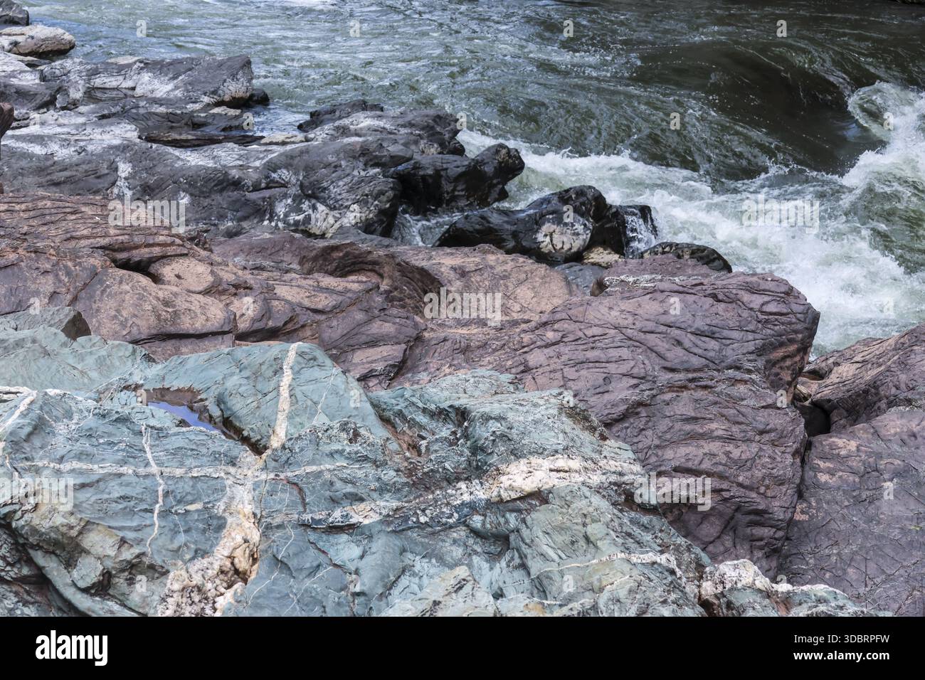 Vista del tranquillo fiume che scorre oltre aspre coste rocciose con struttura in pietra grigia e potente corrente che crea spruzzi di schiuma d'acqua nella natura tranquilla sce Foto Stock