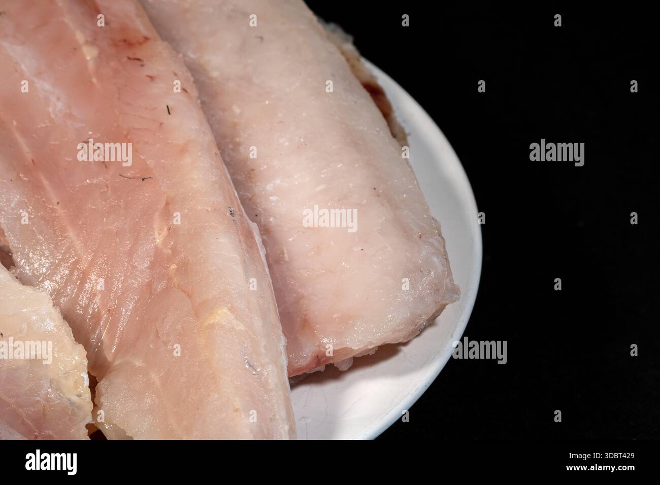 Filetti di nasello crudi su un piatto bianco, pronti per la preparazione Foto Stock