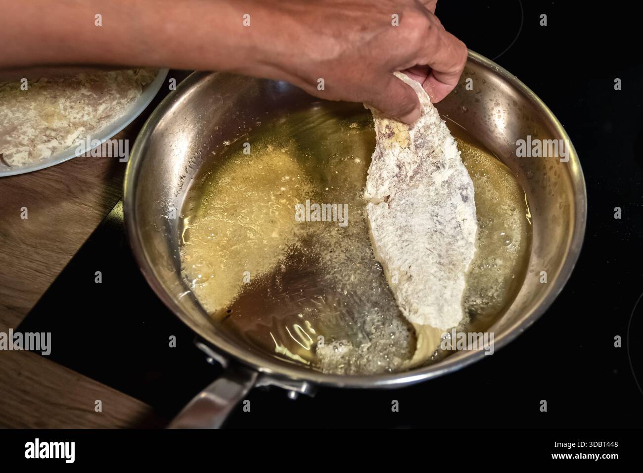 Inserire un filetto di nasello rivestito in olio caldo per friggere Foto Stock