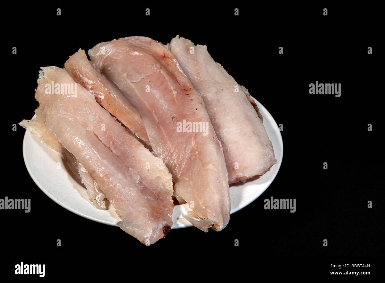 filetto di nasello crudo fresco su piatto bianco su sfondo nero Foto Stock