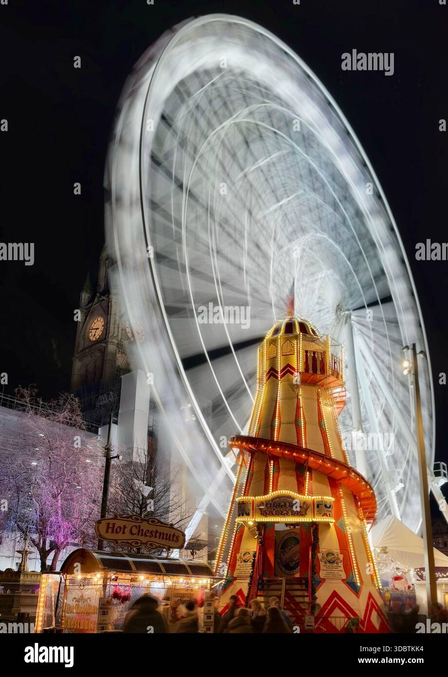 Mercatini di Natale di Manchester. Ruota panoramica (sfocata in movimento) e scivolo Helter skelter illuminato di notte in Albert Square. - Immagine stock catturata con smartphone