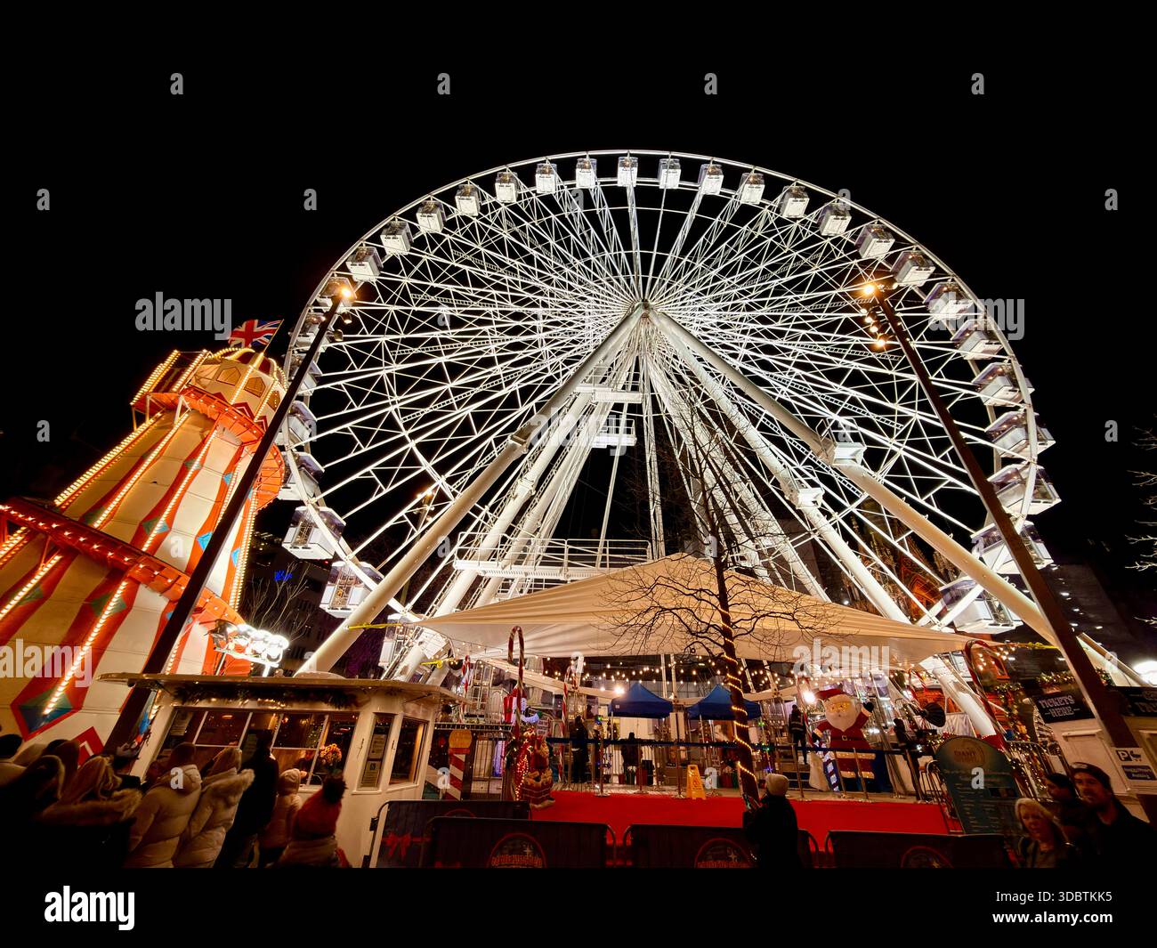 Mercatini di Natale di Manchester. Ruota panoramica e scivolo per skelter illuminati di notte in Albert Square. - Immagine stock catturata con smartphone