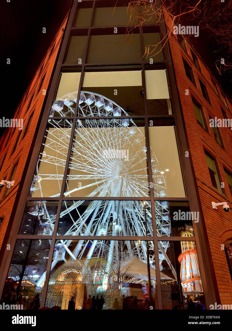Mercatini di Natale di Manchester. Ruota panoramica e scivolo per skelter illuminati di notte in Albert Square riflessi nelle finestre degli uffici - Immagine stock catturata con smartphone