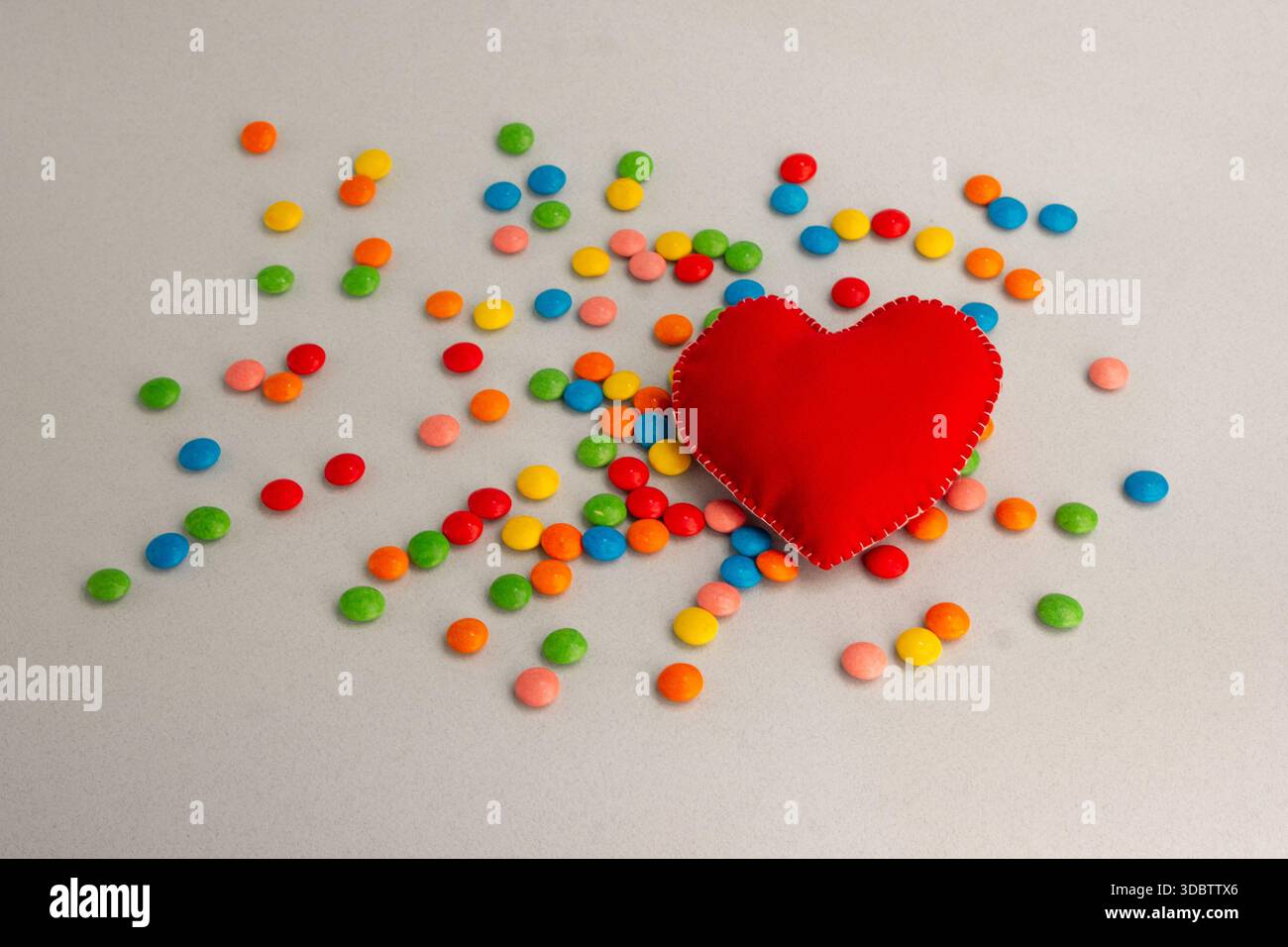 Grande cuore, cuore rosso. Caramelle al cioccolato, piccole e multicolore. Foto Stock