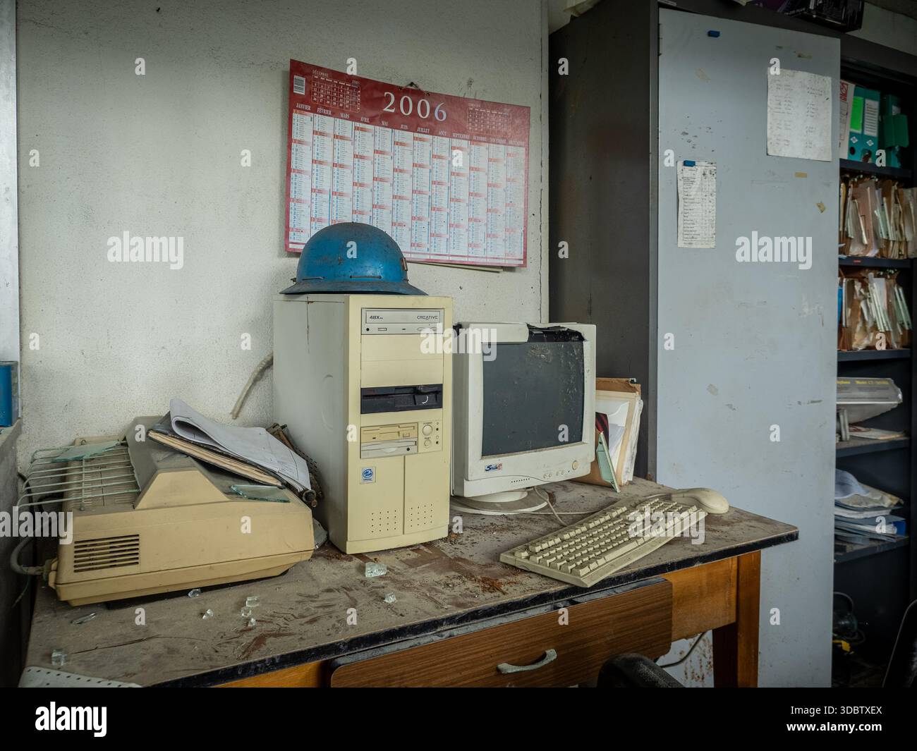 Scrivania da ufficio abbandonata con PC vintage e monitor CRT polveroso, elmetto blu e calendario 2006 Foto Stock