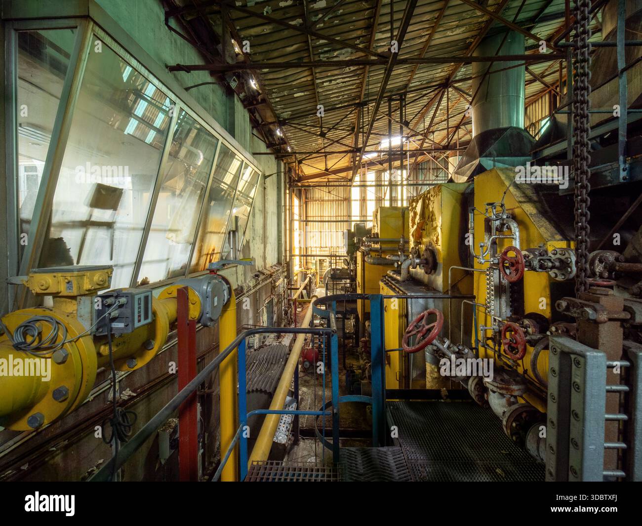 Interni di fabbrica abbandonati con macchinari gialli, tubi arrugginiti e valvole - degrado industriale atmosferico Foto Stock