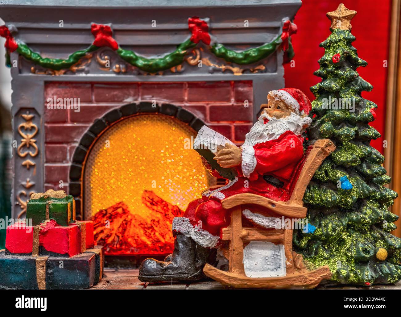 Figurina di Babbo Natale su sedia a dondolo con caminetto con albero di Natale e regali avvolti decorazione natalizia festività festività Capodanno sfondo Foto Stock