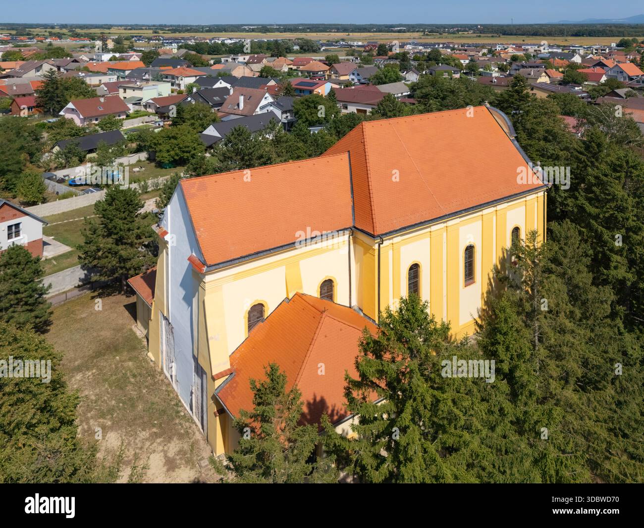 Vista aerea della suggestiva Chiesa di tutti i Santi con il suo tetto arancione e le pareti gialle, annidata tra alberi verdeggianti, Lab, regione di Bratislava, Slovacchia Foto Stock