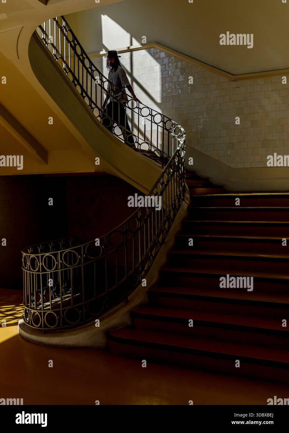 Una persona sta camminando lungo una scala curva con una ringhiera in metallo. La scala è in un edificio con pareti piastrellate e pavimento giallo. Foto Stock