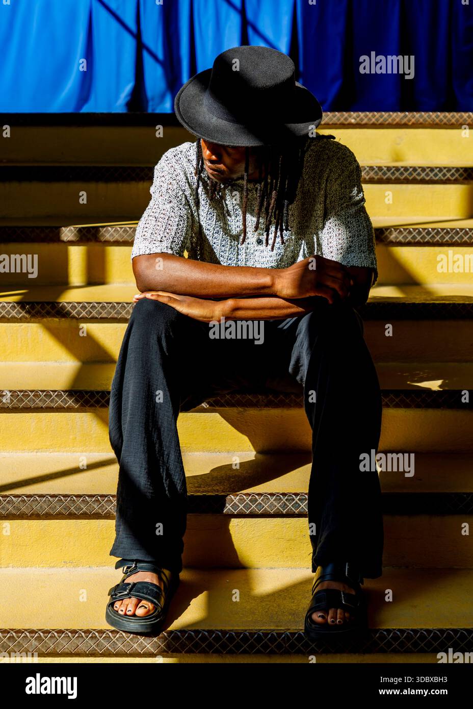 Una persona che indossa un cappello e un sandalo siede su una scala gialla. Foto Stock