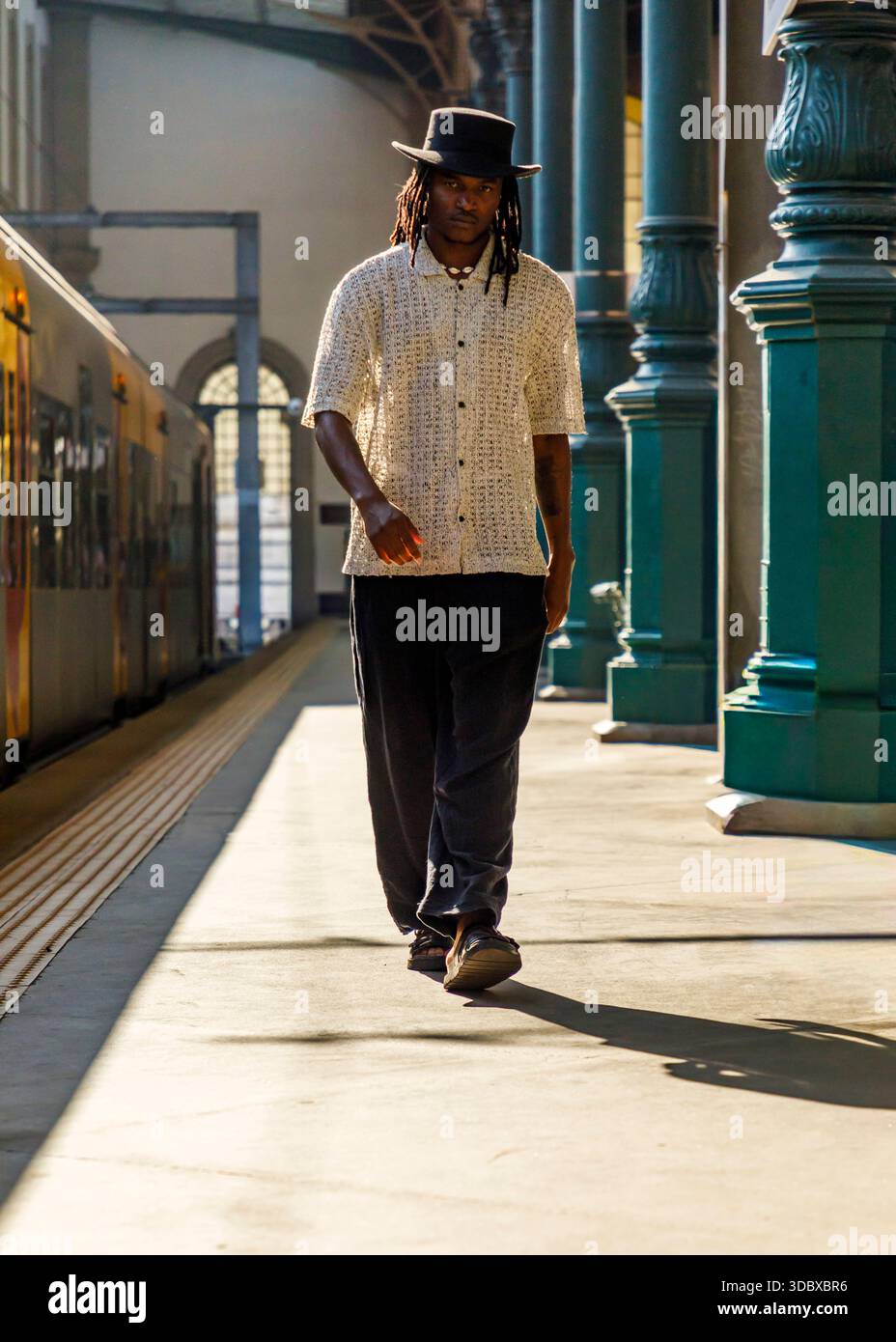 Un uomo che indossa un cappello e una camicia con bottoni cammina su una piattaforma del treno. Foto Stock