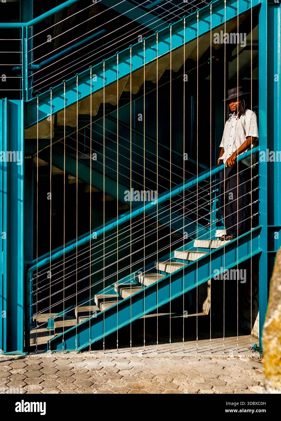 Un uomo che indossa un cappello e una camicia bianca si erge su una scala blu. Foto Stock
