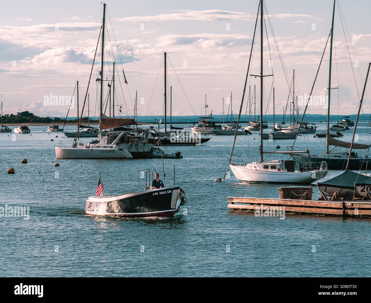 Un piccolo motoscafo si sposta attraverso un campo di ormeggio per barche a vela nel porto di Port Jefferson, Suffolk County, New York, durante le tranquille condizioni estive. Foto Stock