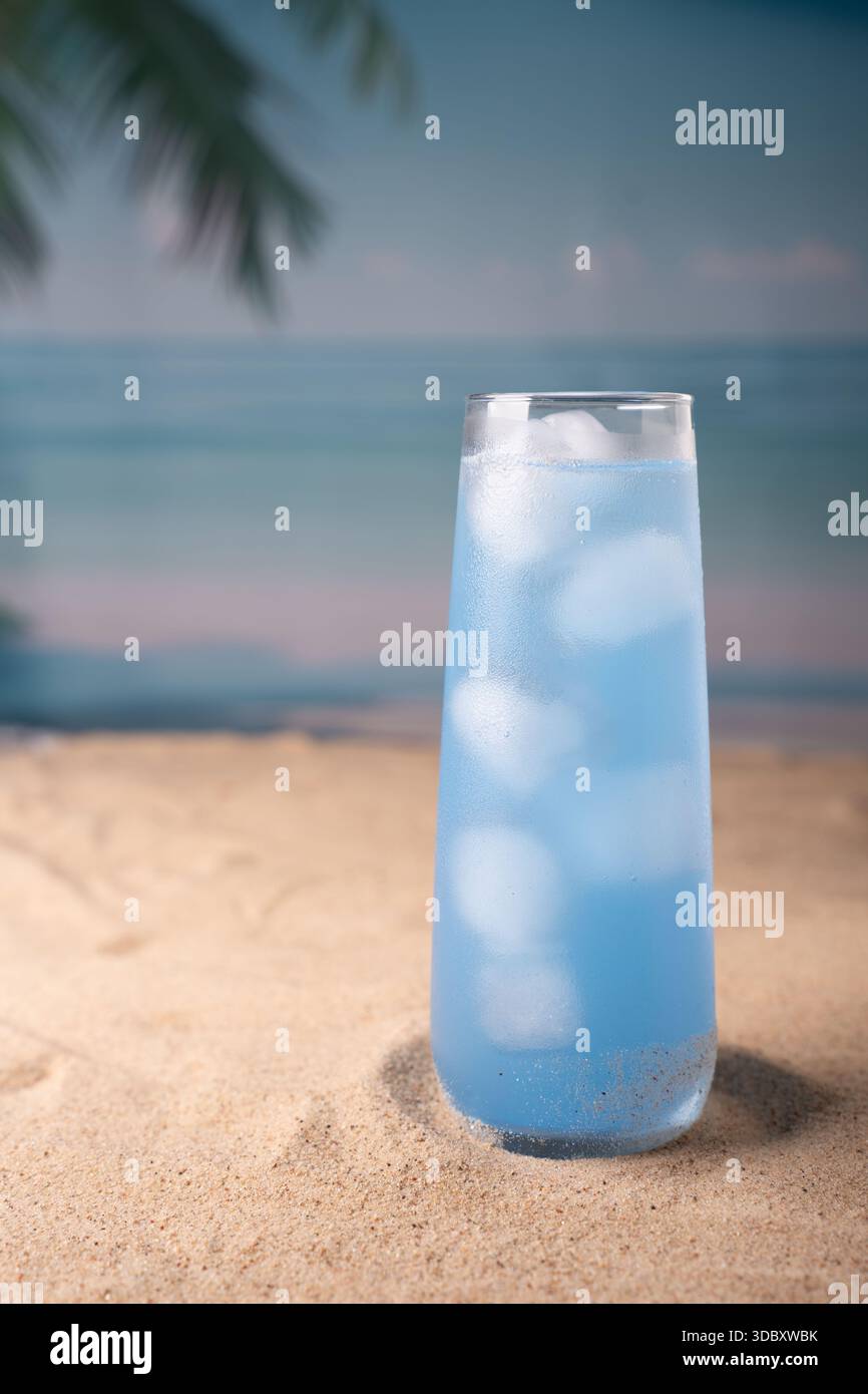 bevande fredde blu in alto vetro adagiate su una spiaggia di sabbia con fronde di palme e orizzonte dell'oceano, evocando serene vibrazioni tropicali e rinfrescante rilassamento estivo Foto Stock