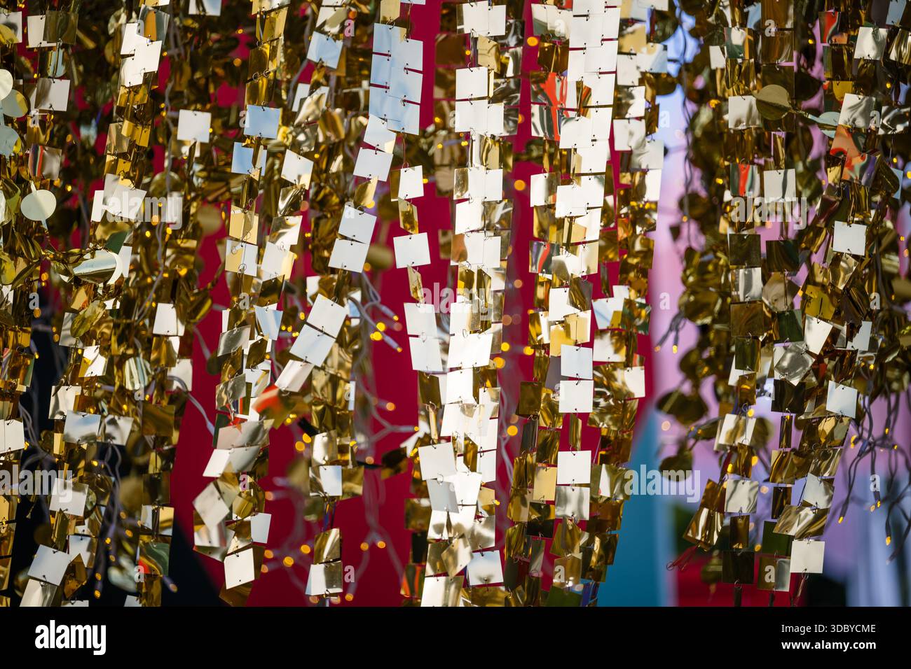 Le decorazioni sospese riflettenti dorate formano un motivo festivo astratto con luci soffuse che si illuminano sullo sfondo Foto Stock
