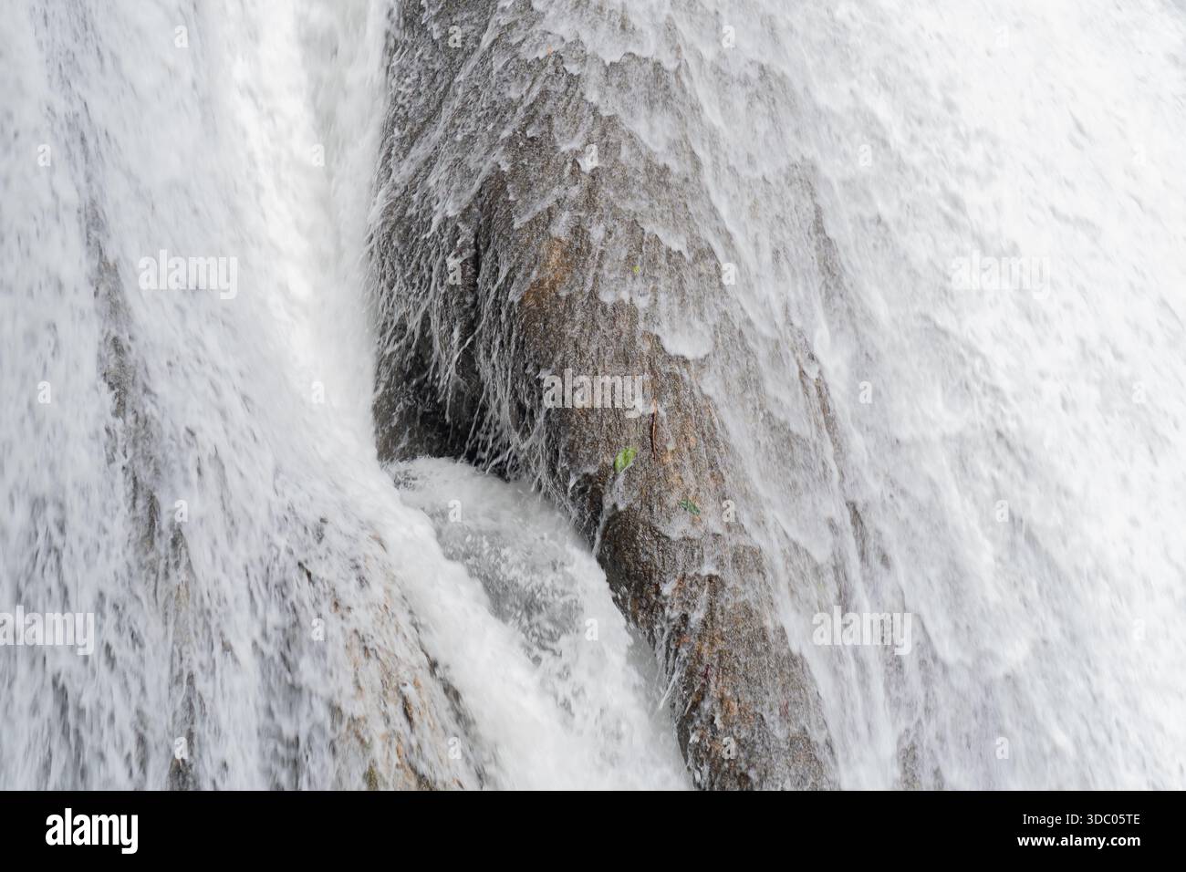 Primo piano dettagliato della cascata di acqua bianca sul viso di roccia marrone testurizzata in luce naturale Foto Stock