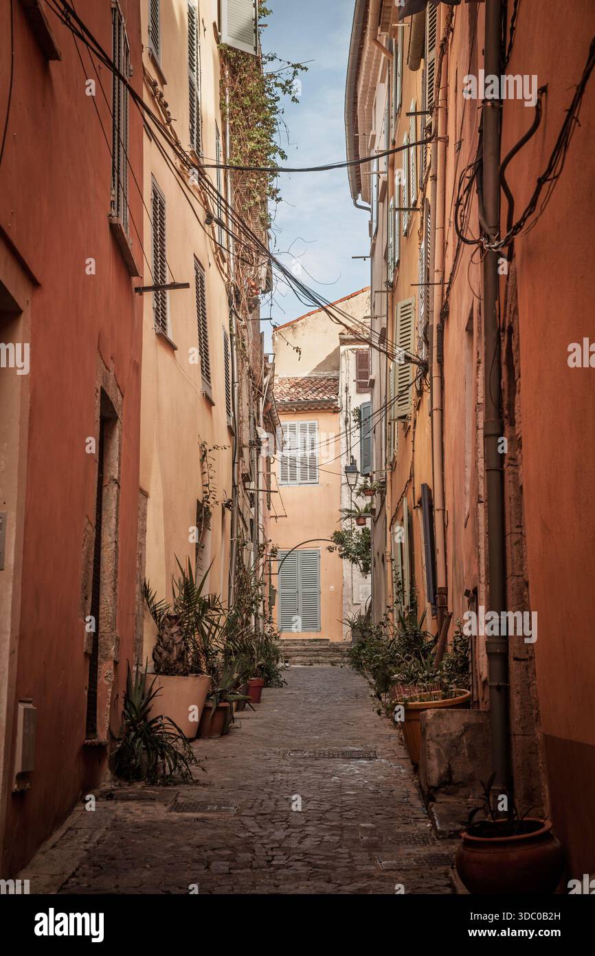 Vista verticale lungo una stradina stretta della Vieux Hyeres, costa Azzurra, Francia, con facciate color pastello, persiane e piante in vaso, che mostrano un tipico provenzale Foto Stock