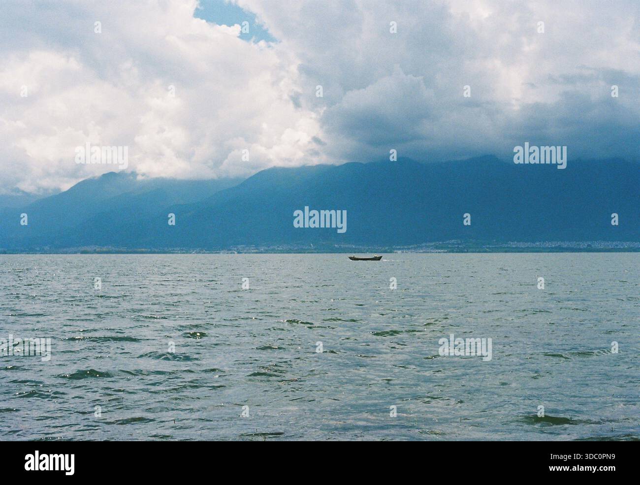 Una tranquilla fotografia cinematografica del lago Erhai a Dali, con dolci onde in primo piano e una piccola barca che si sposta vicino all'orizzonte. Foto Stock