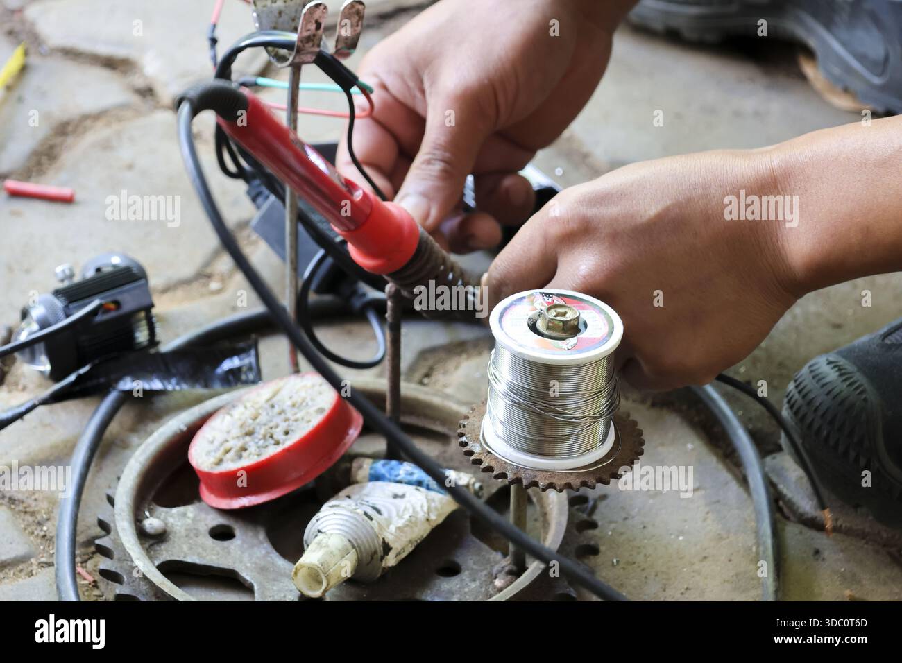 Mani di tecnici concentrati che fissano il filo elettrico con saldatore riscaldato e banco di lavoro con filo per saldatura fuso con precisione, meticolosa e precisa Foto Stock