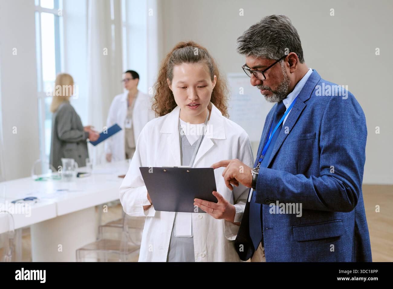 Uomo di mezza età e giovane donna asiatica adulta discutere rapporto medico Foto Stock