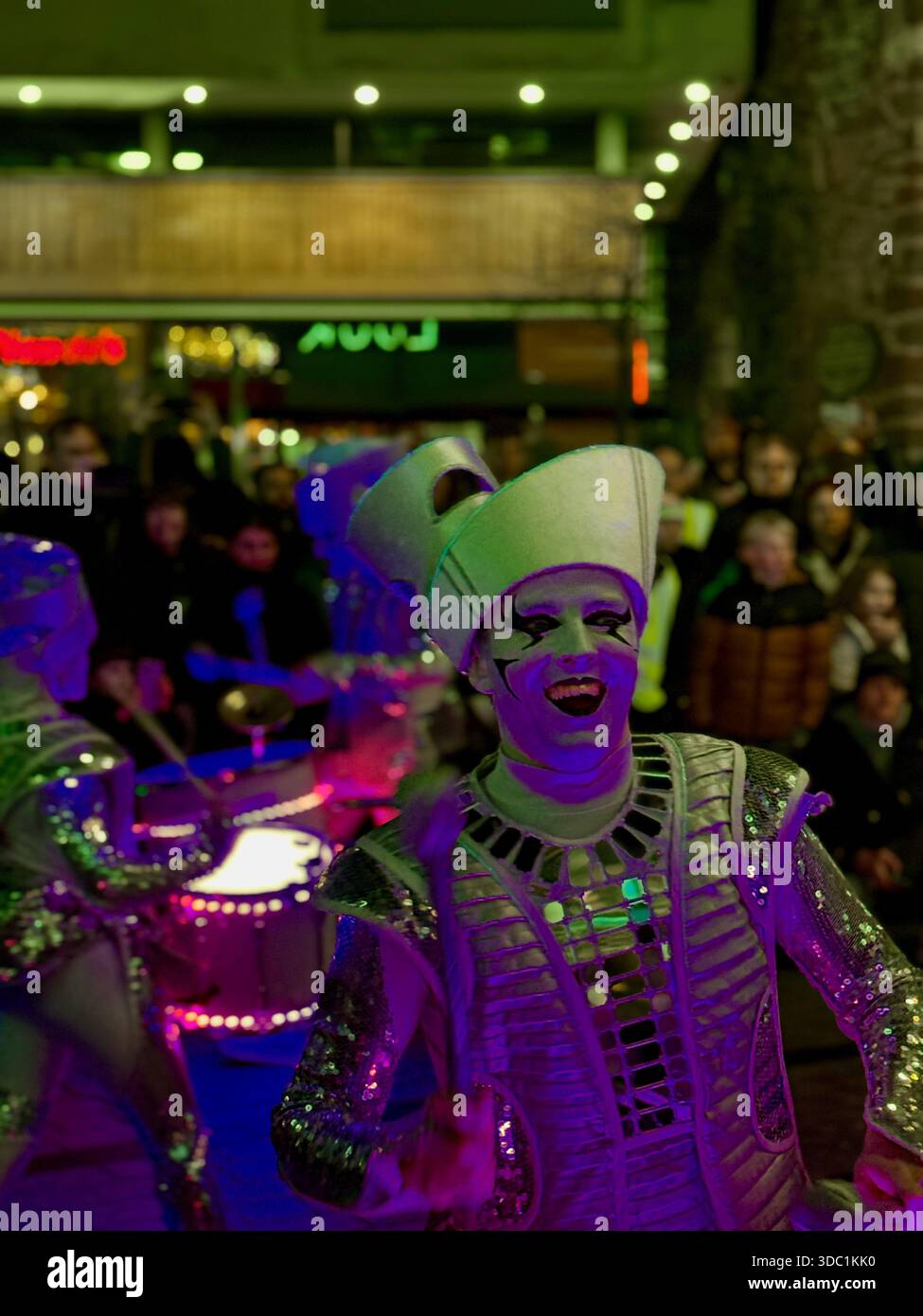 SCINTILLA! Batteristi a LED che si esibiscono in un evento natalizio a Princesshay, Exeter, con costumi illuminati e una folla vivace. - Immagine stock catturata con smartphone