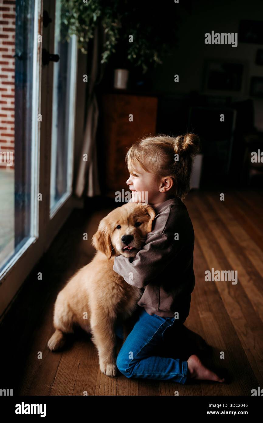 ragazza che abbraccia il cucciolo dorato del retriver in una casa Foto Stock