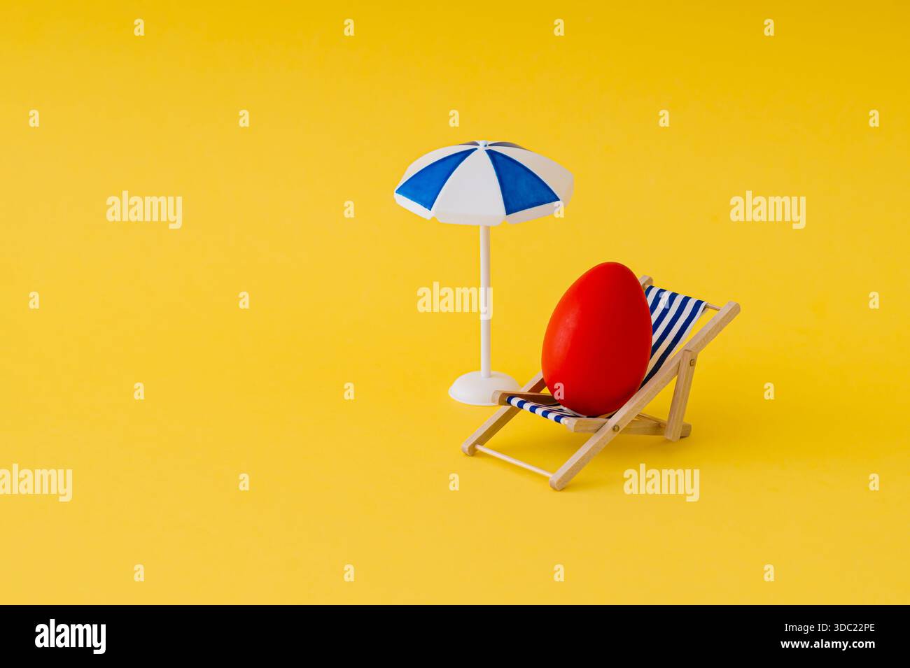 Uovo di Pasqua rosso su sdraio con ombrellone su sfondo giallo. Concetto di Pasqua. Layout creativo per le festività. Estetica pasquale. Copia spazio. Foto Stock