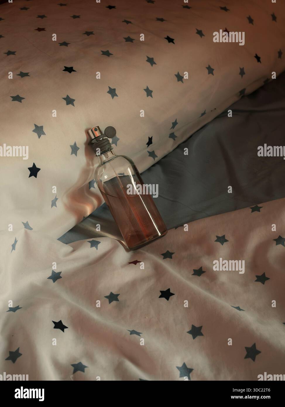 Bottiglia di profumo in vetro appoggiata sul letto con lenzuola bianche. Fragranza modello mockup. Foto Stock