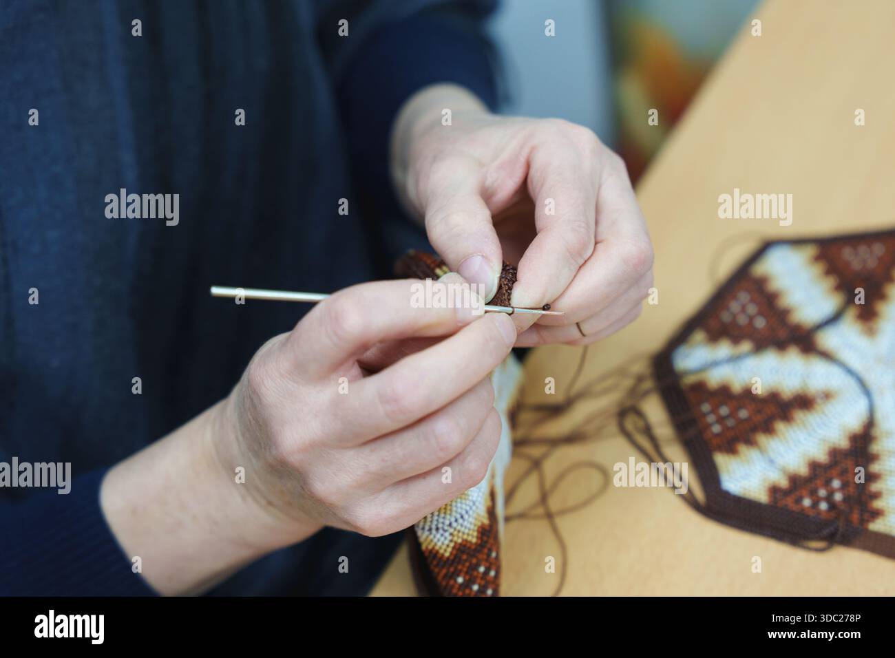 Avvicinati le mani di un'artigiana utilizzando un gancio a uncinetto per creare una borsa con perline e motivi geometrici. Foto di alta qualità Foto Stock