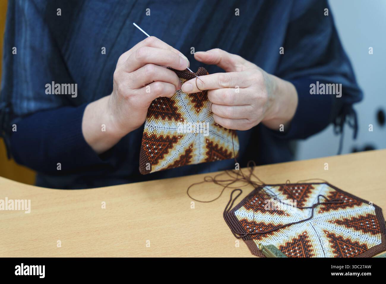 Avvicinati le mani di un'artigiana utilizzando un gancio a uncinetto per creare una borsa con perline e motivi geometrici. Foto di alta qualità Foto Stock