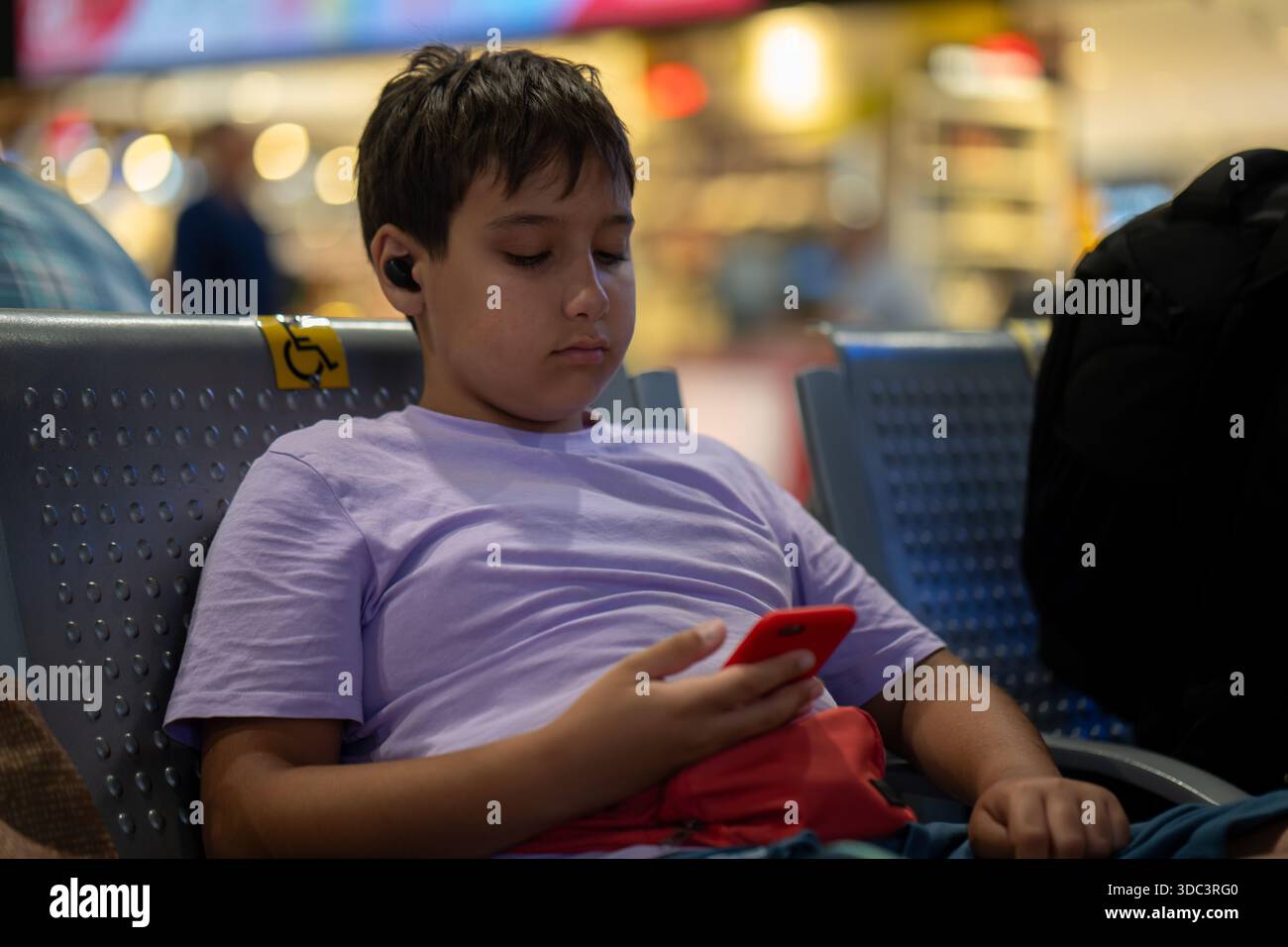 Ragazzo seduto a usare il telefono e ad ascoltare gli auricolari. Foto di alta qualità Foto Stock