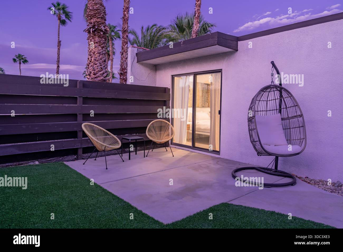 Patio della camera da letto in stile moderno della metà del secolo, sedie Acapulco a filo metallico, poltrona a forma di uovo appesa, al crepuscolo serale con palme Foto Stock