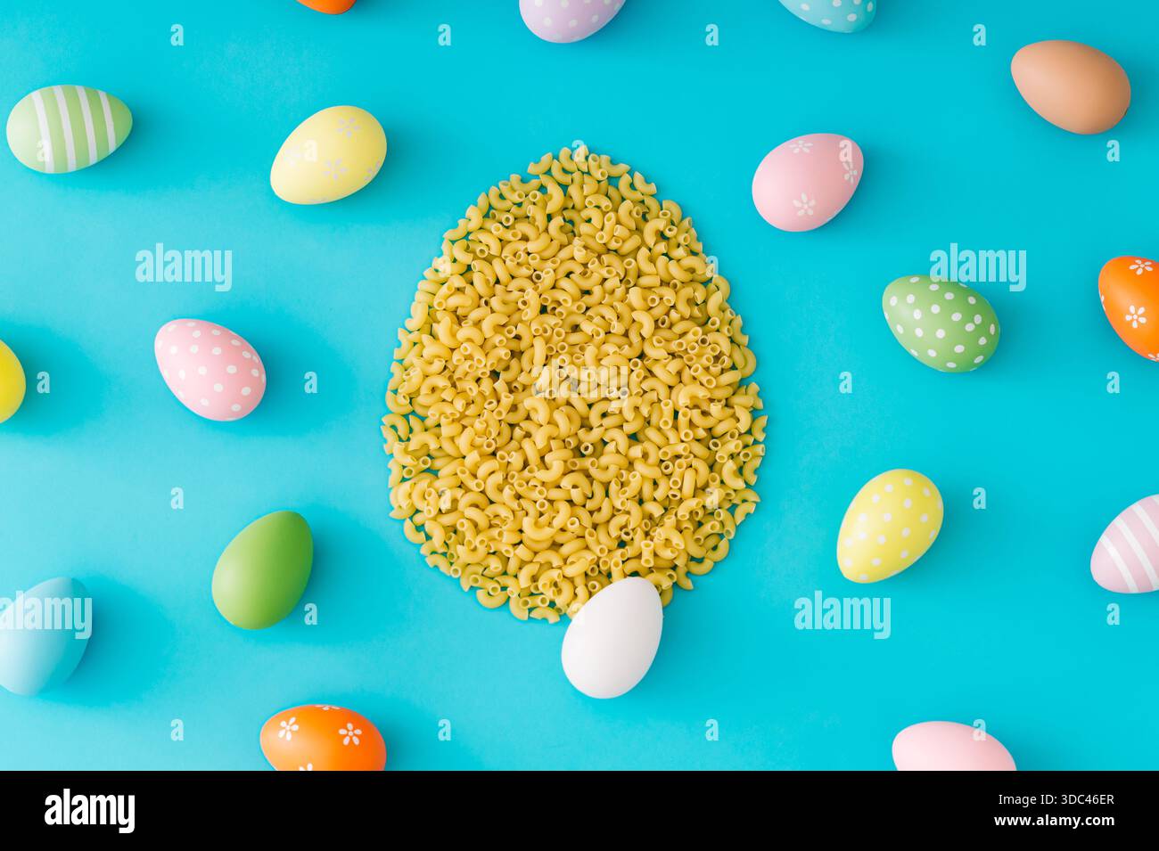 Motivo colorato a base di uova di Pasqua di vari colori a forma di uovo di Pasqua a base di pasta cruda a gomito su sfondo azzurro. Foto Stock